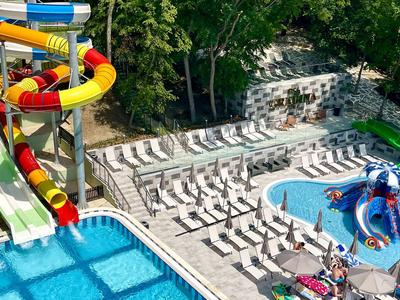 Parc aquatique avec plusieurs toboggans, deux piscines et des transats dans un cadre verdoyant.