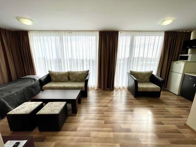 Modern eingerichtetes Wohnzimmer mit Sofa, Sesseln, Tisch und großen Fenstern mit Vorhängen.