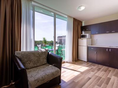 Hell eingerichtetes Hotelzimmer mit Küchenzeile und Balkon mit Ausblick.