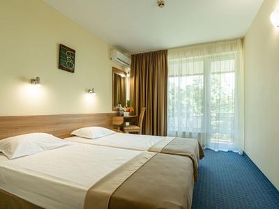 Ein Hotelzimmer mit zwei Einzelbetten, blauem Teppich und Balkon mit Vorhängen.