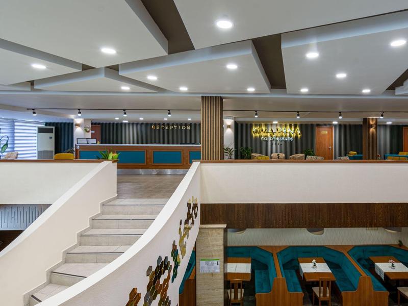 Modern eingerichtete Hotelhalle mit Rezeption, Treppe und Essbereich mit Tischen und Sitzbänken.