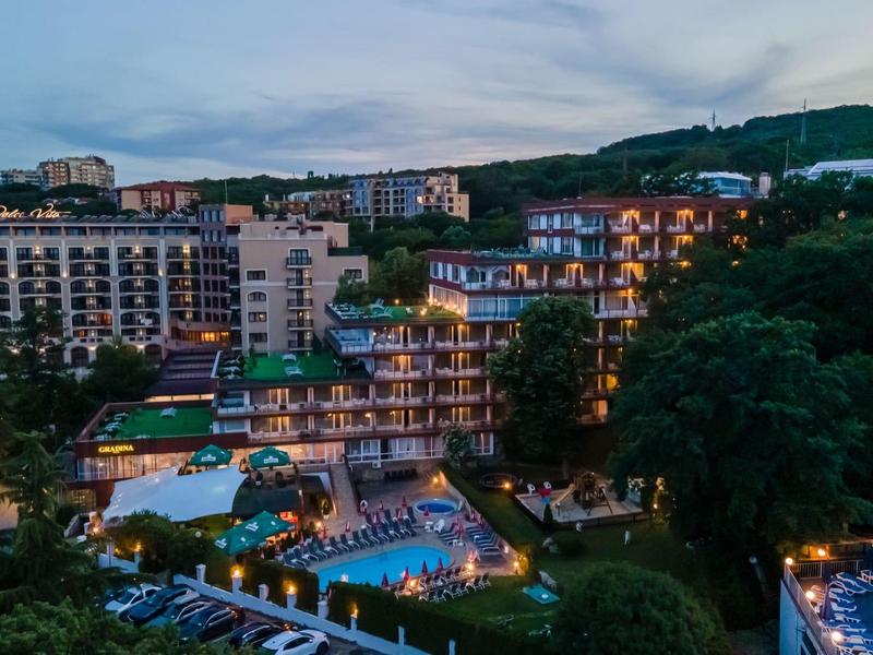Beleuchtetes Hotel mit Pool und umliegender grüner Landschaft bei Abenddämmerung.