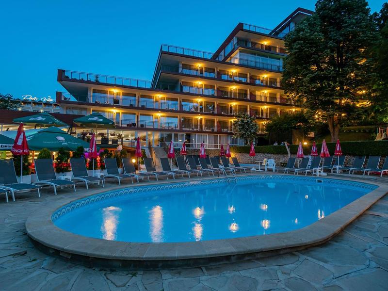 Beleuchteter Außenpool vor einem mehrstöckigen Hotelgebäude bei Abenddämmerung.