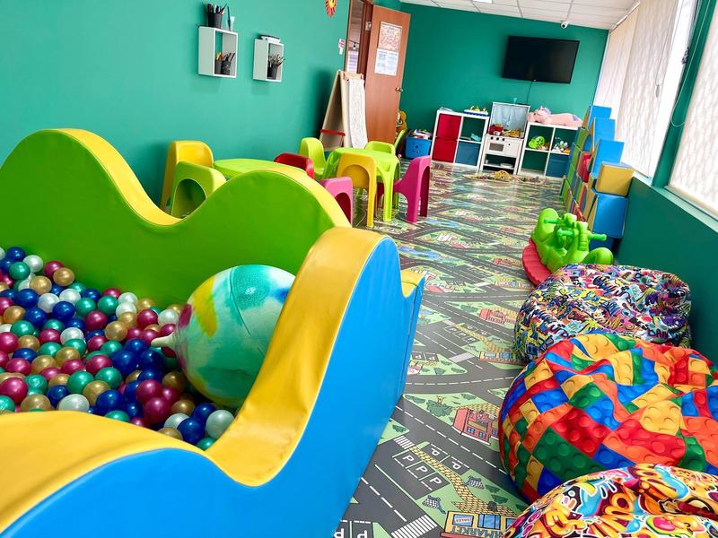 Buntes Kinderspielzimmer mit Bällen, Sitzsäcken und Spielzeug vor grünem Hintergrund.