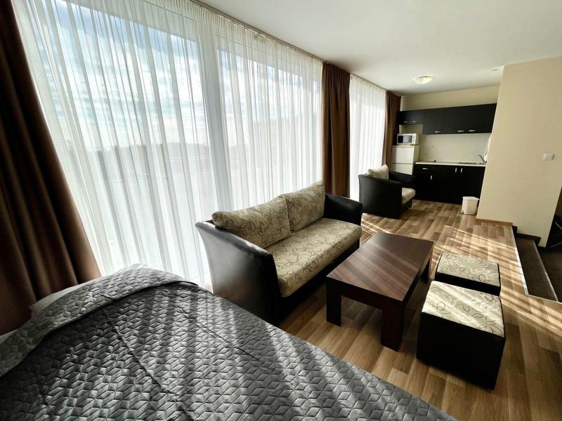 Helles Hotelzimmer mit Sofa, Couchtisch, Betten und großen Fenstern mit Vorhängen.