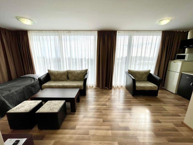 Modern eingerichtetes Wohnzimmer mit Sofa, Sesseln, Tisch und großen Fenstern mit Vorhängen.