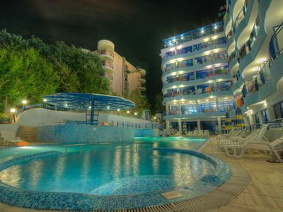 Beleuchteter Hotelpool bei Nacht mit Liegestühlen und modernem Gebäude im Hintergrund.