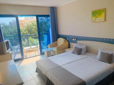 Jasny pokój hotelowy z podwójnym łóżkiem, balkonem i miejscem do siedzenia z widokiem na drzewa.