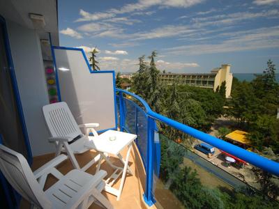 Balkon z białymi krzesłami i niebieską balustradą z widokiem na ulicę i drzewa.