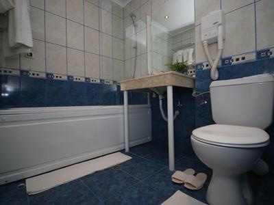 Mała łazienka z wanną, toaletą, umywalką i suszarką do włosów na ścianie.