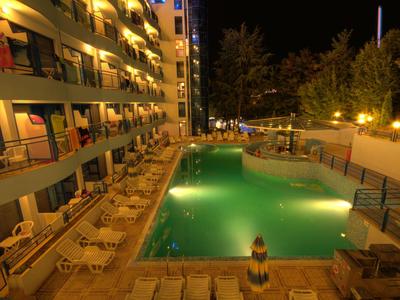 Beleuchteter Hotelpool in der Nacht mit Liegestühlen und Balkonen