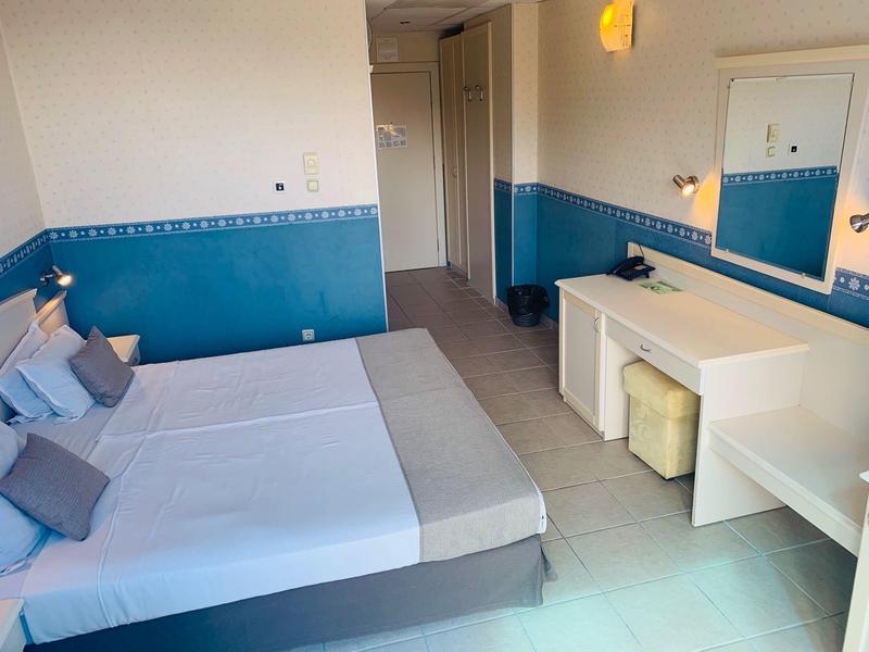 Jasny pokój hotelowy z łóżkiem podwójnym, niebiesko-białymi ścianami i biurkiem z lustrem.