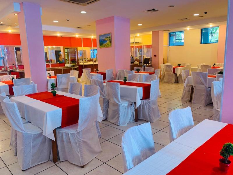 Jasna restauracja hotelowa z białymi pokrowcami na krzesła i czerwonymi bieżnikami stołowymi.