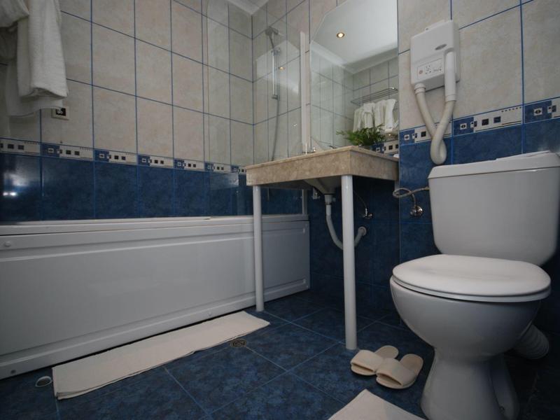 Mała łazienka z wanną, toaletą, umywalką i suszarką do włosów na ścianie.