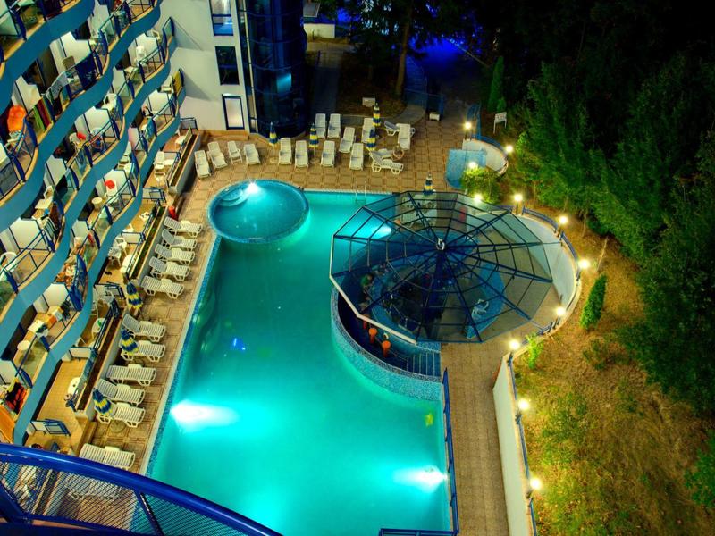 Oświetlony basen hotelowy z leżakami i barem, otoczony zielenią nocą.