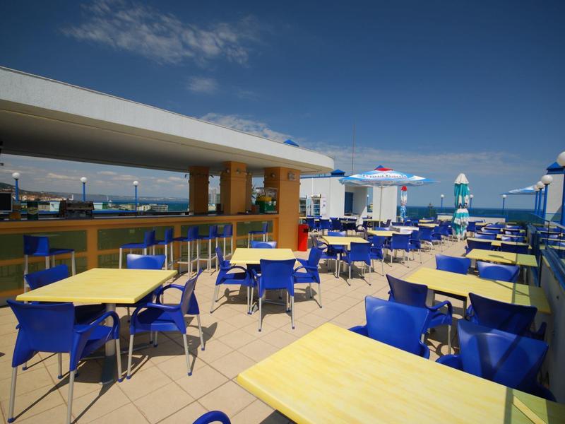 Zewnętrzny taras z żółtymi stołami i niebieskimi krzesłami pod czystym niebem.