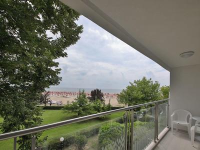 Balcony with glass railing, two white chairs, and view of green park and buildings.