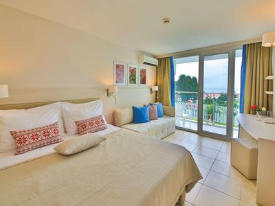 Jasny pokój w hotelu z podwójnym łóżkiem, częścią wypoczynkową i balkonem z widokiem na zieleń.