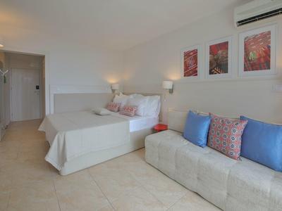 Nowoczesny pokój hotelowy z dwoma łóżkami, sofą, jasnymi ścianami i minimalistycznym wystrojem.