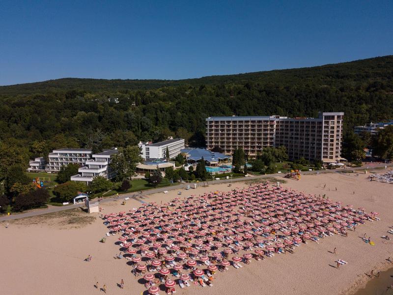 Plaża z czerwonymi parasolami i hotelami w tle na tle zalesionych wzgórz