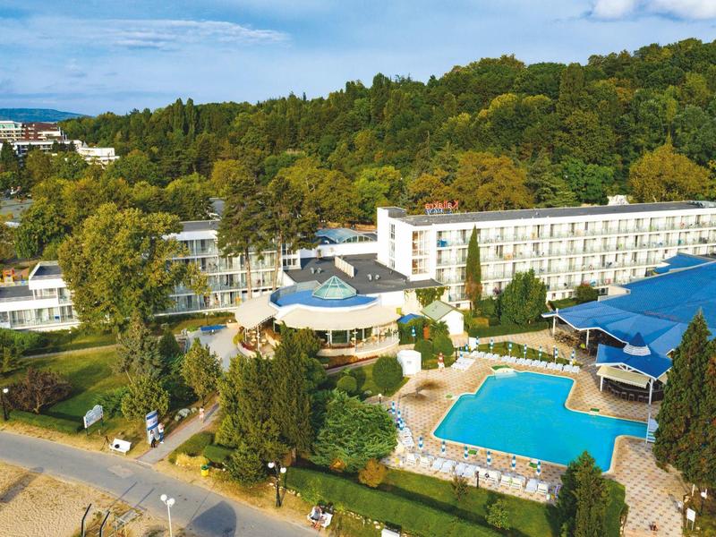 Kompleks hotelowy z dużym basenem na zewnątrz, otoczony zielonymi drzewami i bezpośrednim dostępem do plaży.