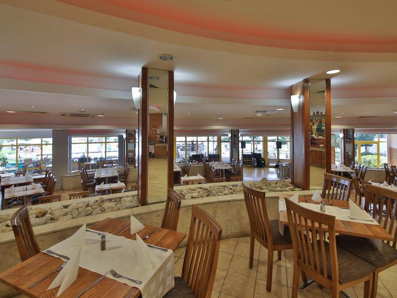 Jasno urządzona część hotelu lub restauracji z drewnianymi stołami i krzesłami obok dużych okien.