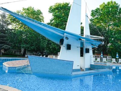 Moderní bazén s elegantní modrou plachtovou konstrukcí vedle stromů a lehátek.