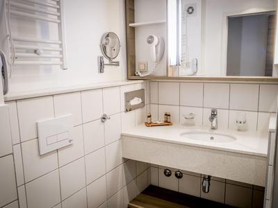 Czysta łazienka hotelowa z umywalką, lustrem i suszarką do włosów.