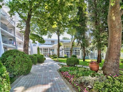 Dlažební cesta skrz hotelovou zahradu s stromy a květinami.