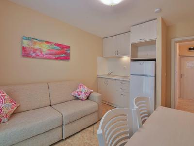 Salon hotelowy z beżową sofą, kompaktową kuchnią i kolorową dekoracją na ścianie.