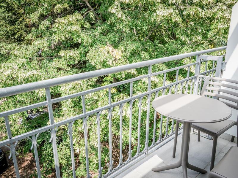 Balkon z białą balustradą, stołem i krzesłem z widokiem na zielone liście.