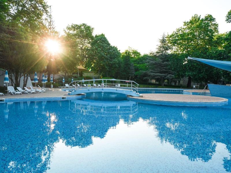 Basen zewnętrzny z mostkiem, leżakami i drzewami o zachodzie słońca.