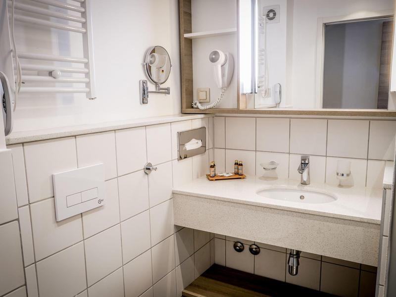 Czysta łazienka hotelowa z umywalką, lustrem i suszarką do włosów.