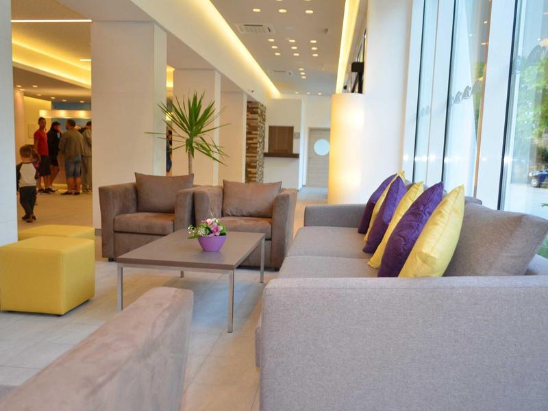 Jasny salon hotelowy z sofami, żółtymi poduszkami i dużym oknem z widokiem na zewnątrz.