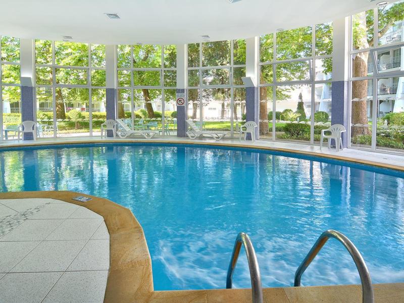 Basen kryty z dużymi oknami z widokiem na drzewa i budynki.