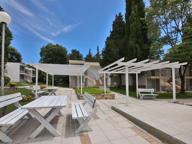 Nowoczesny taras z białymi meblami i pergolami w zielonym hotelu pod niebieskim niebem.