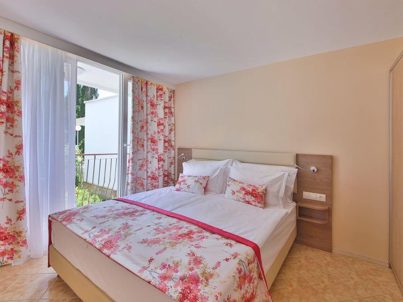 Jasny pokój z podwójnym łóżkiem, kwiecistą pościelą i balkonem z widokiem.