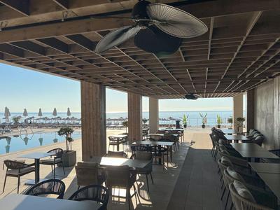 Covered terrace with tables and chairs overlooks pool and sea.