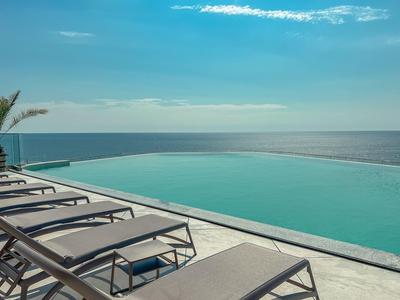 Basen typu infinity z leżakami z widokiem na spokojne morze pod błękitnym niebem.