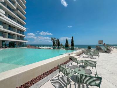 Nowoczesny basen typu infinity z widokiem na morze obok hotelu i leżaków na tarasie.