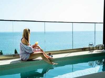 Kobieta siedzi na brzegu basenu z widokiem na morze pod czystym niebem.