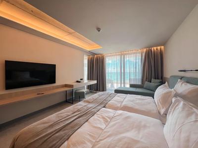 Nowoczesny pokój hotelowy z dużym łóżkiem, telewizorem, biurkiem i balkonem z widokiem na zewnątrz.