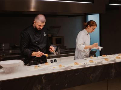 Szef kuchni i kucharka przygotowują kilka przystawek na talerzach w profesjonalnej kuchni.