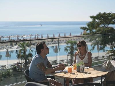 Para siedzi przy stole na tarasie z widokiem na basen i morze.