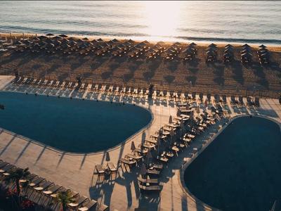 Wieczorna scena na plaży z basenem, leżakami i parasolami nad morzem.