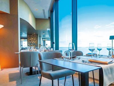 Nowoczesna restauracja z dużymi oknami, nakrytymi stolikami i jasnym światłem dziennym.