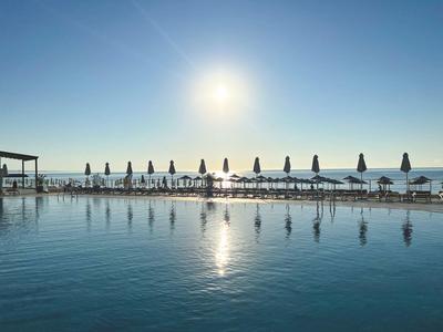 Widok na basen z parasolami i ludźmi na plaży pod słonecznym niebem.