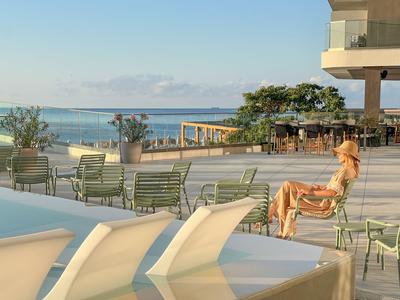Woman in summer dress sitting by pool overlooking sea and beach bars.