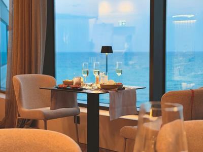 Mesa elegante con copas de vino y vista al mar a través de una gran ventana en un restaurante.