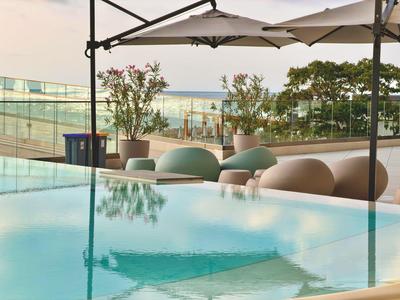 Piscina moderna de hotel con sombrillas y asientos, vista al mar de fondo.